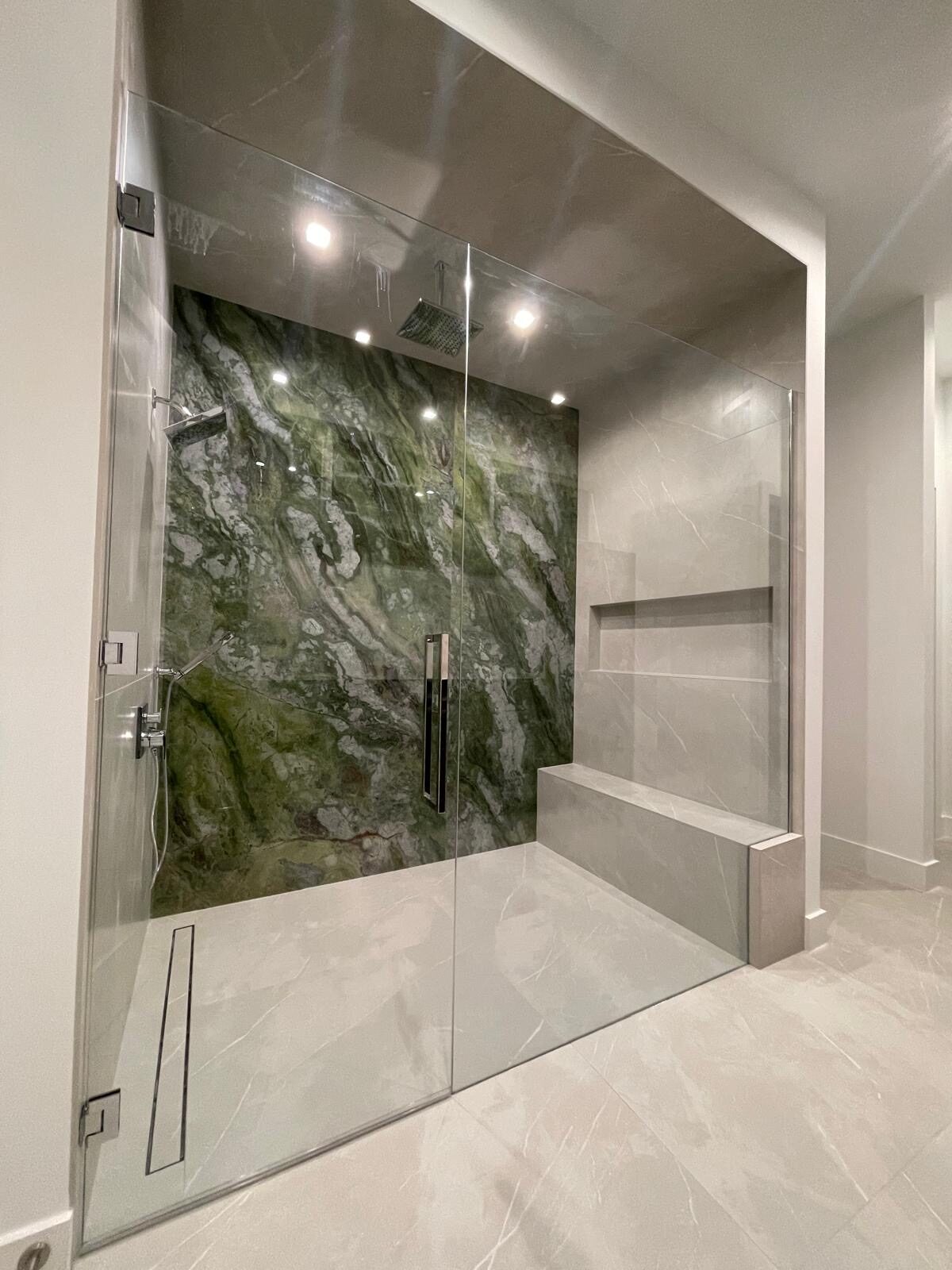 Glass steam shower with green marble and bench
